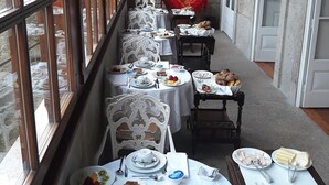 Un long couloir où sont disposées des tables préparées pour le petit-déjeuner, avec des nappes blanches, des assiettes remplies de nourriture et des chaises blanches.