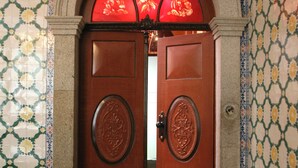 Une porte en bois ornée de motifs complexes, encadrée dans un mur recouvert de carreaux disposés selon un motif géométrique.
