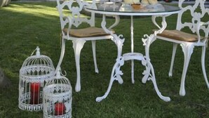 Une table blanche décorée, avec des chaises et deux cages à oiseaux contenant des bougies, le tout installé dans un jardin.