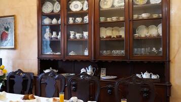 Una mesa de comedor dispuesta con alimentos para el desayuno, rodeada de armarios de madera ornamentados con puertas de cristal que exhiben vajilla.