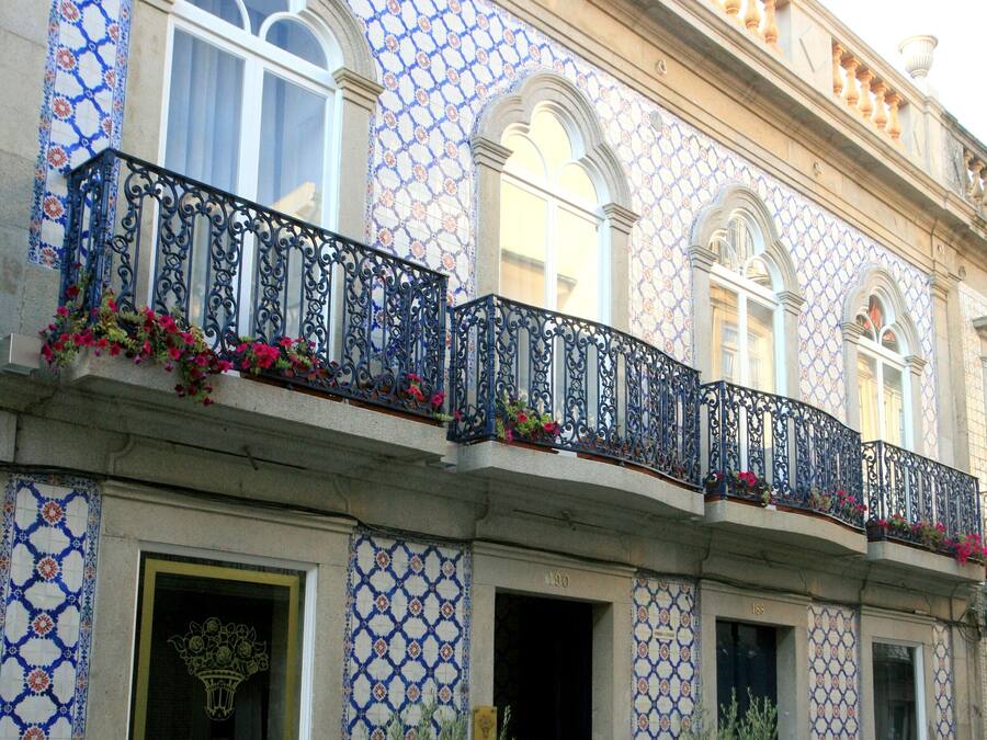 A building with blue and white patterned tiles, a balcony with black wrought iron railings, and potted plants in front.
