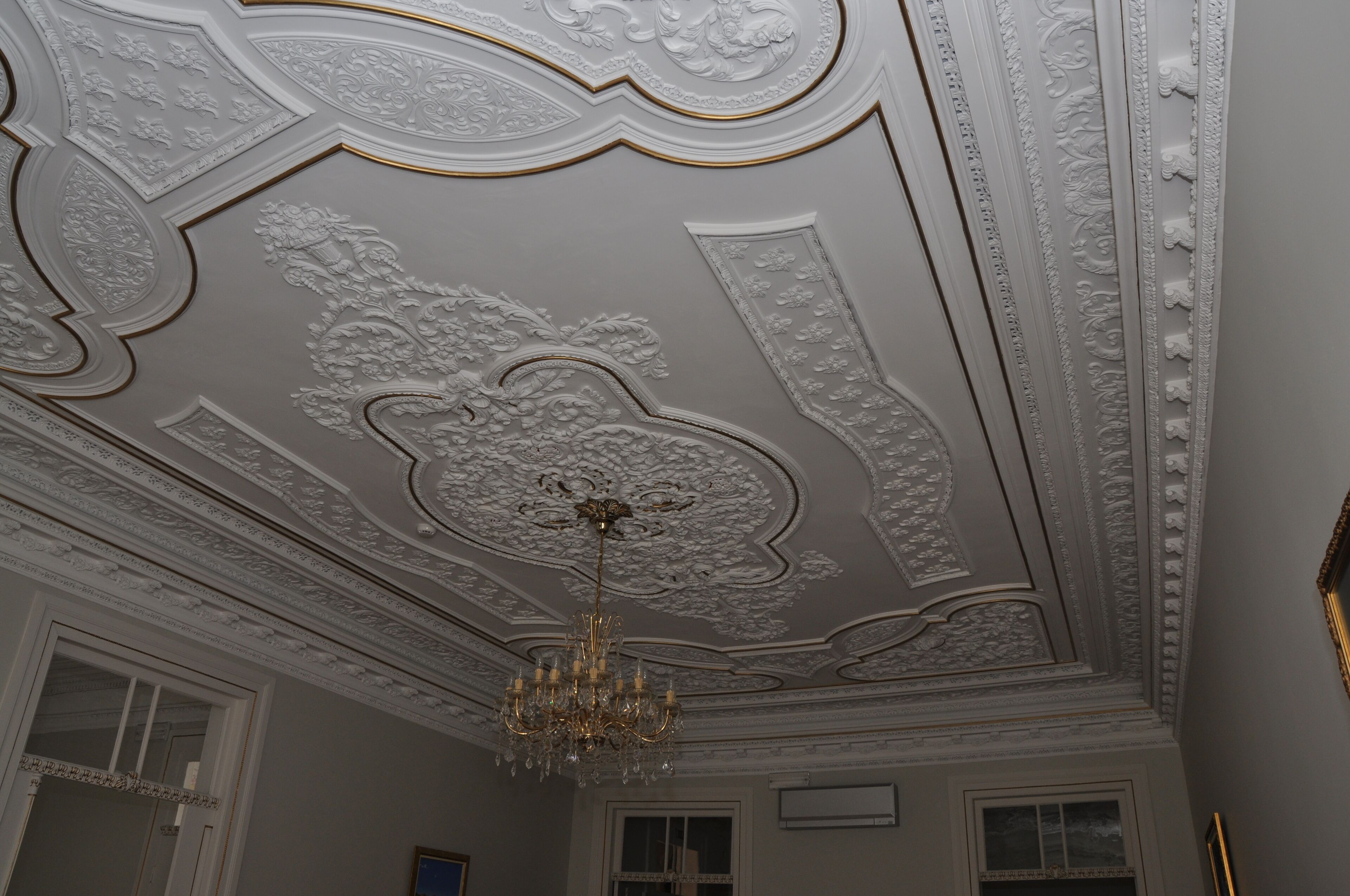 Quarto com detalhes ornamentais no teto e um candelabro.