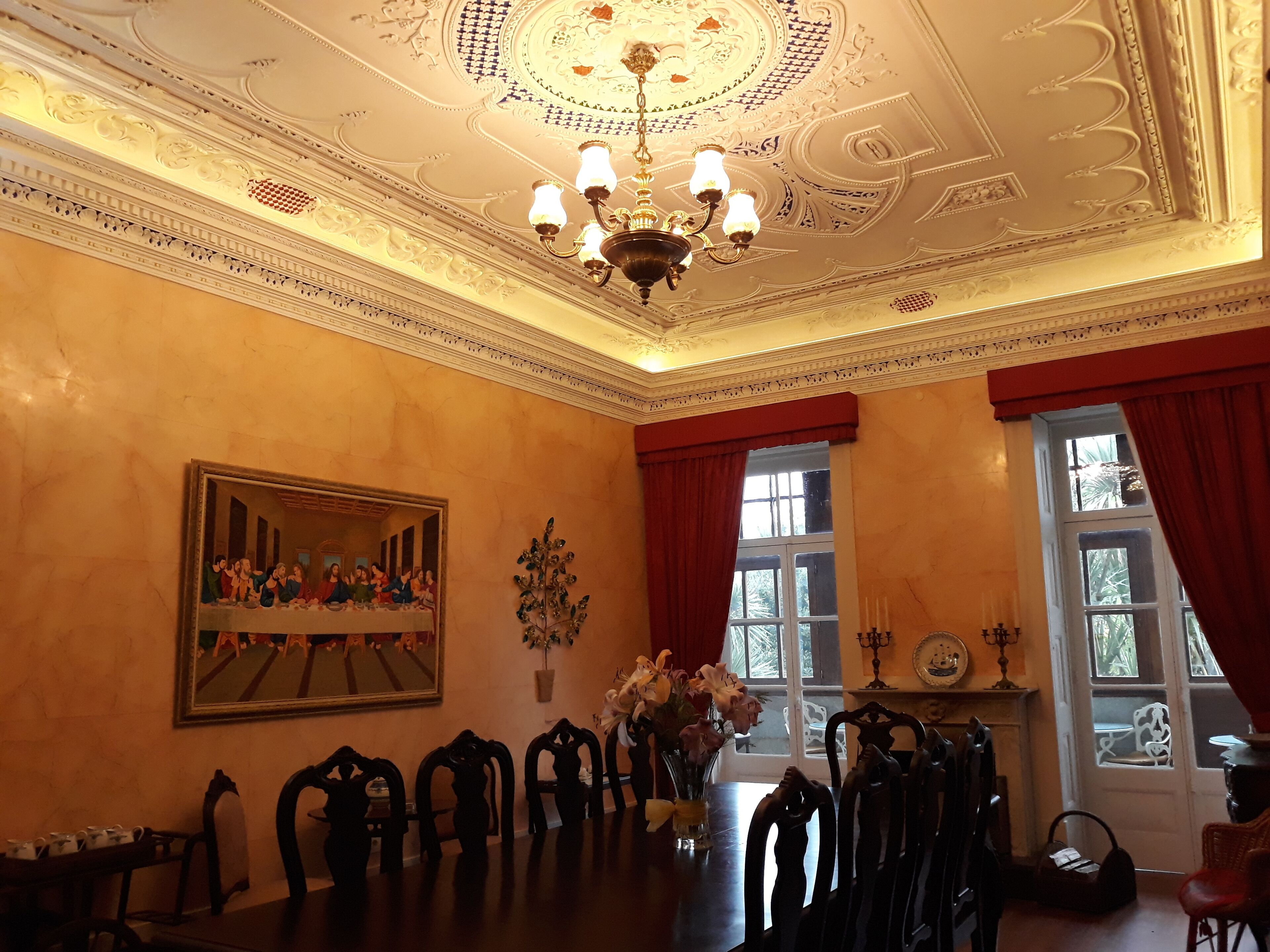 A dining room with a chandelier, a large painting, and a vase of flowers.