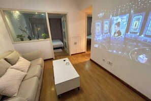 Una sala de estar moderna con un sofá, una mesa de centro y una pantalla de proyección mostrando a una persona.