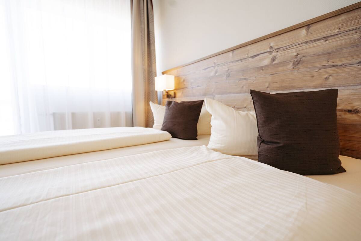 Una habitaci ón de hotel con cabecera de madera, cama con ropa de cama blanca y ventana con cortinas.