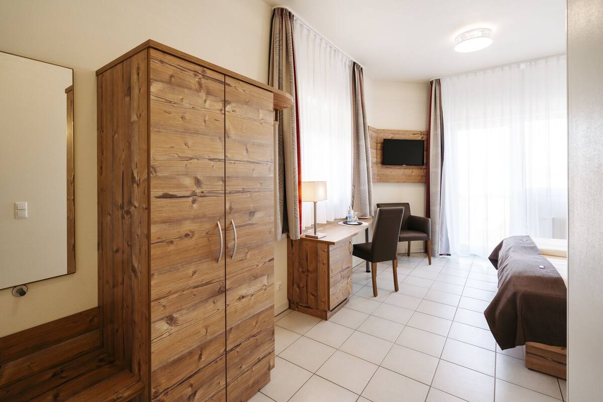 Una habitación de hotel con un armario de madera, un escritorio con una silla, una cama y un televisor montado en la pared.