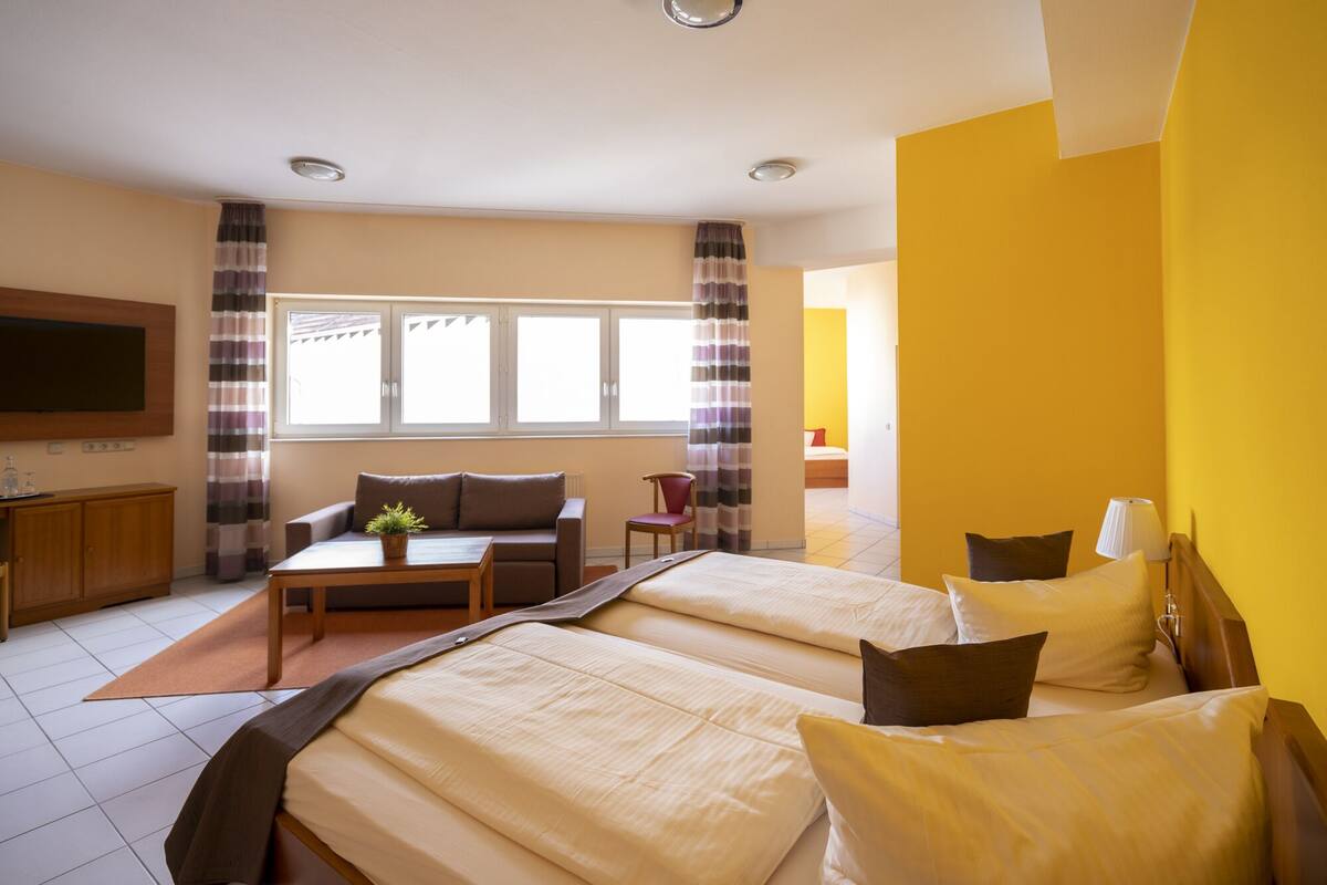 Una habitación de hotel con dos camas, un sofá, una mesita y un televisor.