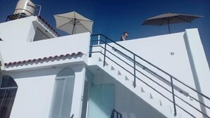 A white building with a staircase, a rooftop air conditioning unit, and two umbrellas. - La Casa de Ana (Arequipa)
