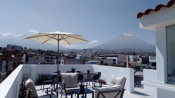 A rooftop terrace with outdoor furniture, a large umbrella, and a view of a mountain. - La Casa de Ana (Arequipa)