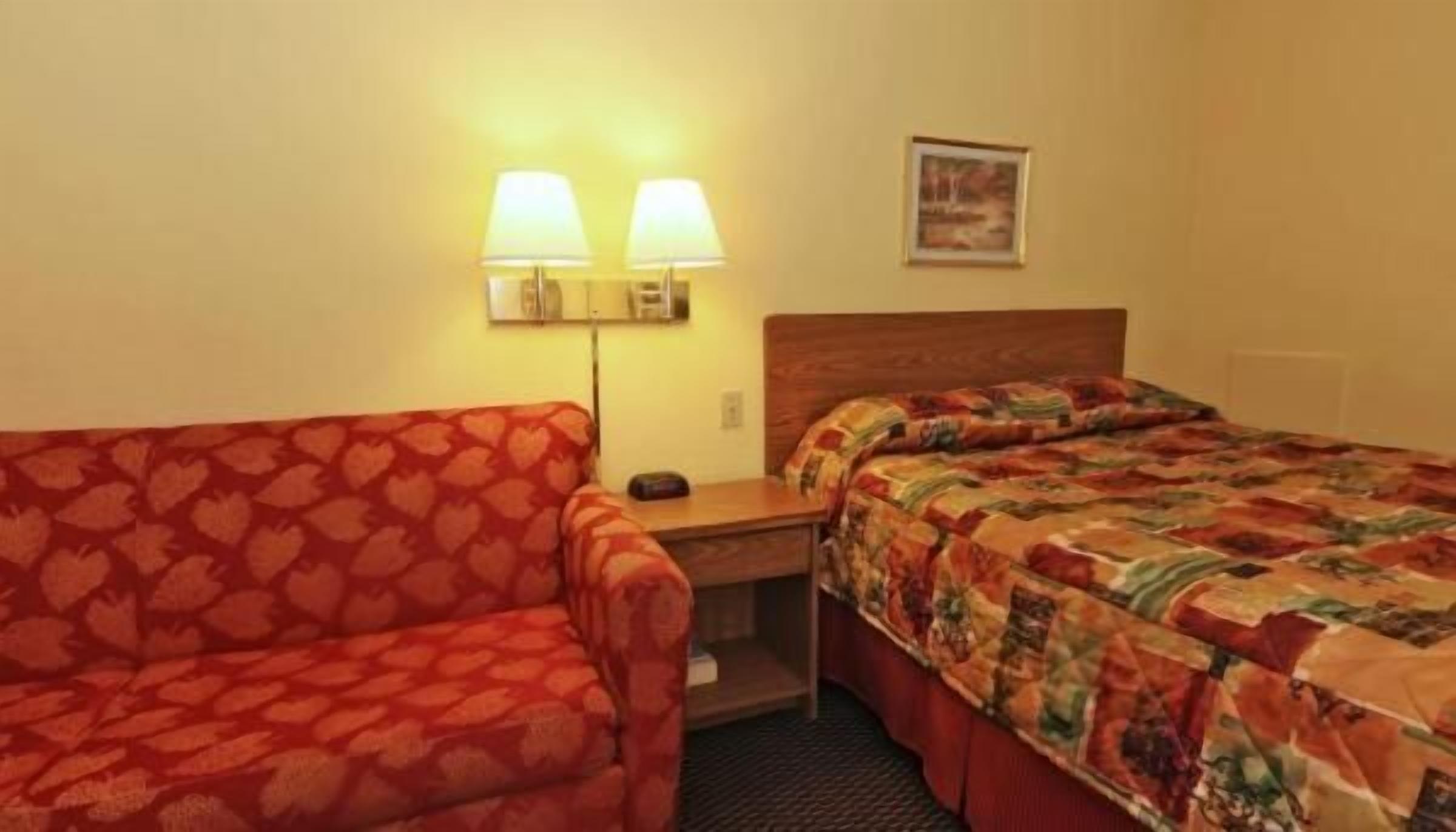 A hotel room with a bed, a sofa, a nightstand, and two wall-mounted lamps.