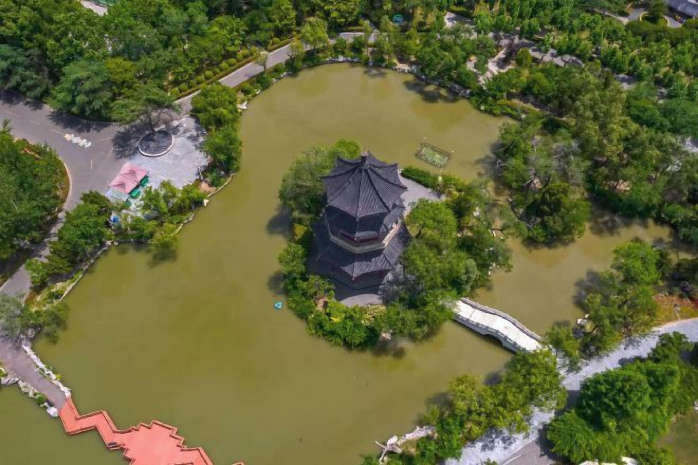 A pagoda surrounded by a pond with a bridge, surrounded by greenery.