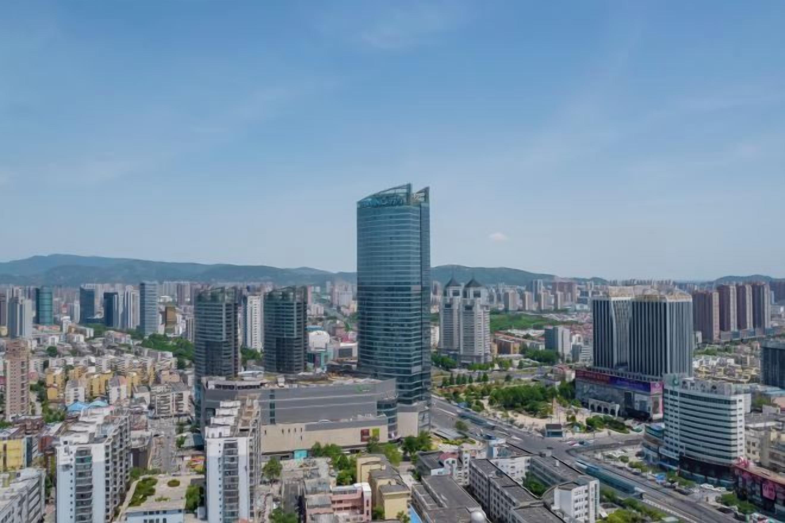 A cityscape with modern high-rise buildings, a clear sky, and a distant mountain range.