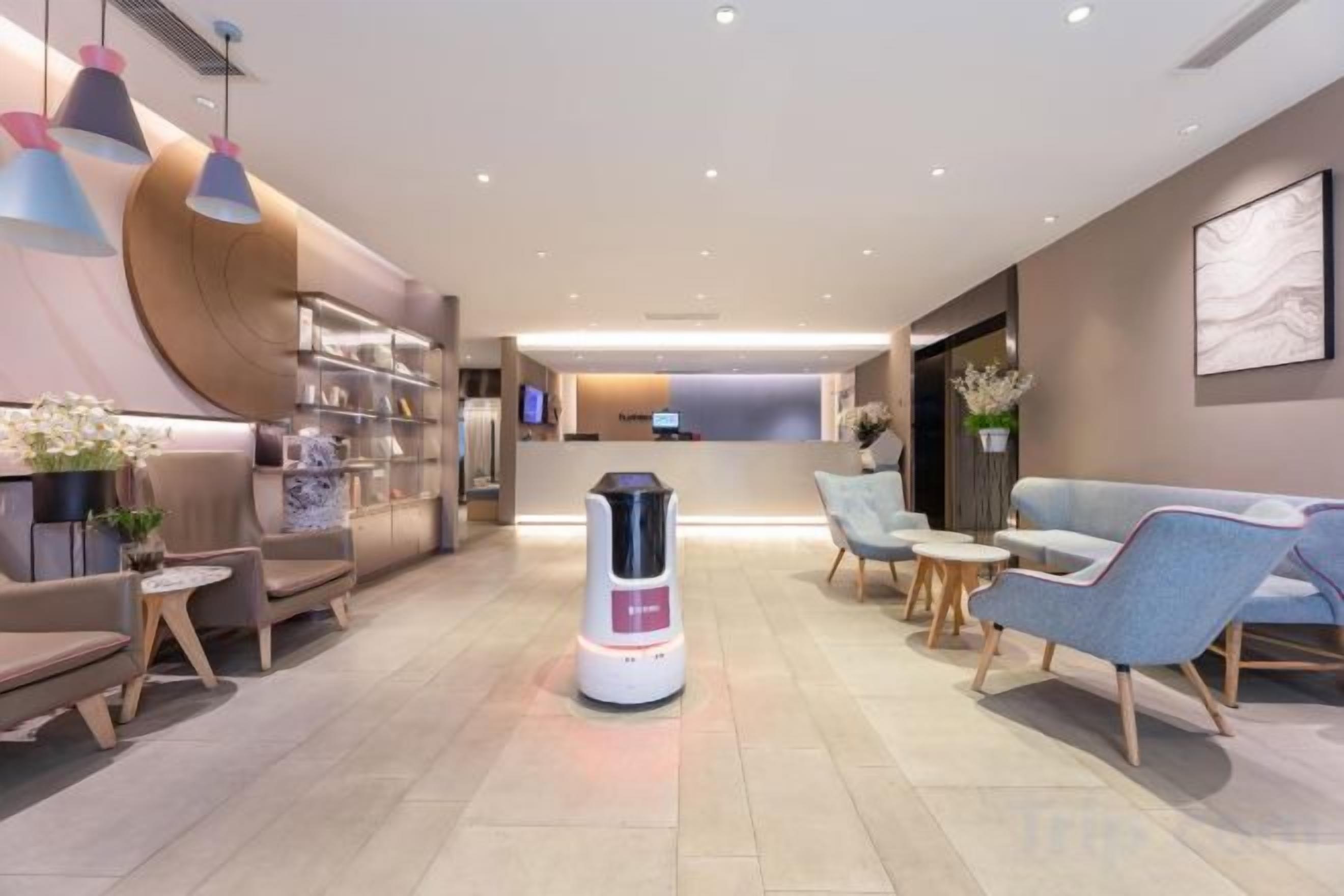 A modern hotel lobby with seating areas, a reception desk, and a self-service kiosk.