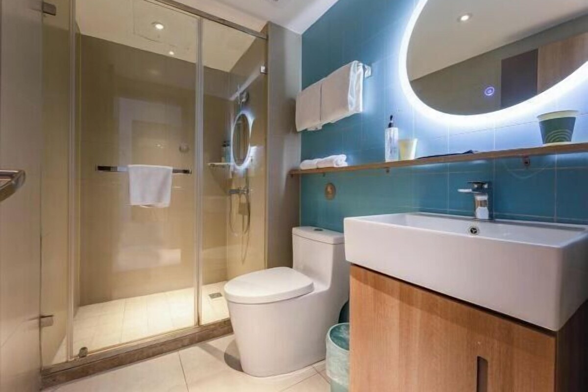 Un baño moderno con ducha envuelta en vidrio, inodoro blanco, lavamanos con espejo y una pared de acento azul.