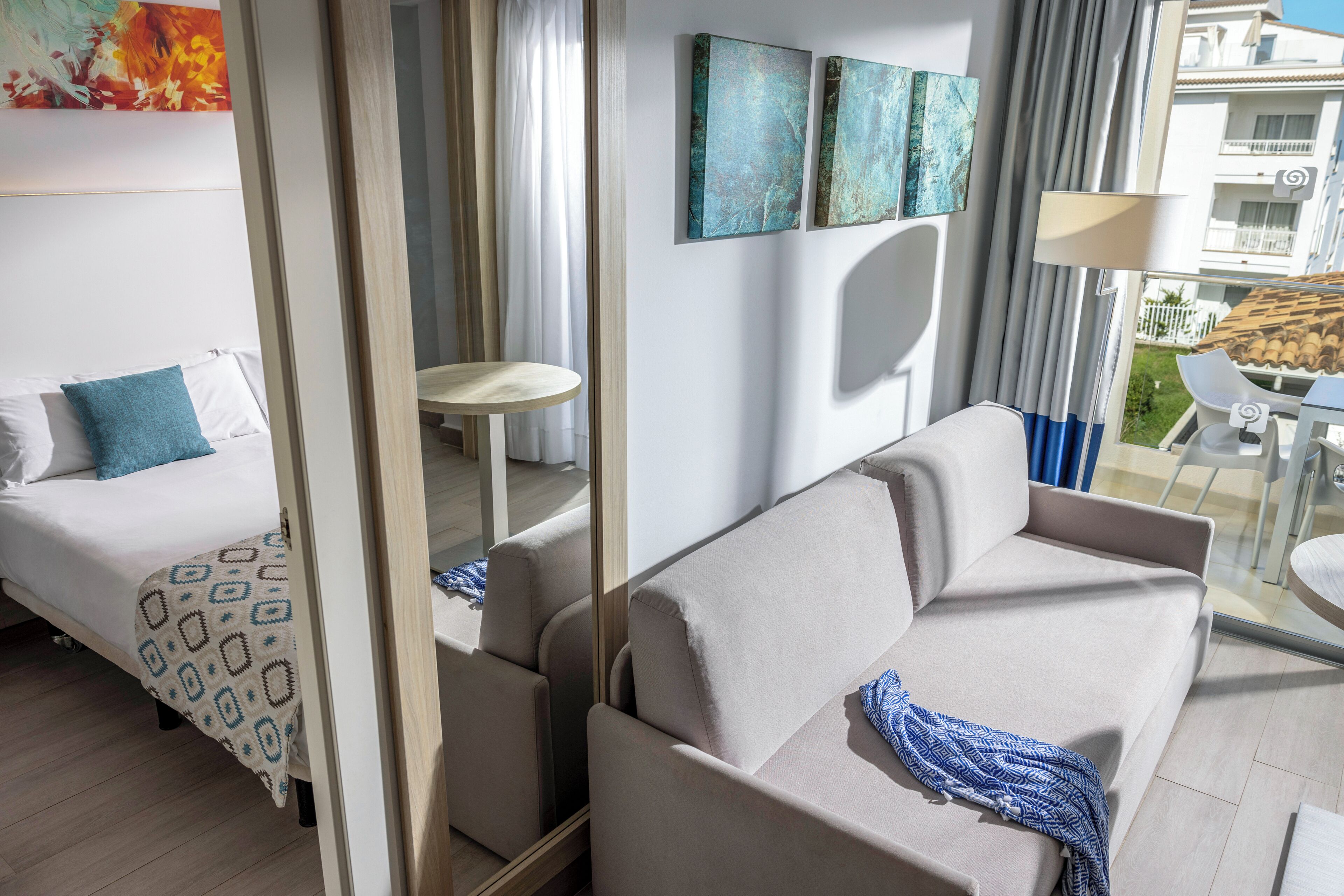 Een moderne hotelkamer met een bed, een slaapbank, een klein rond tafeltje en een balkon met uitzicht.