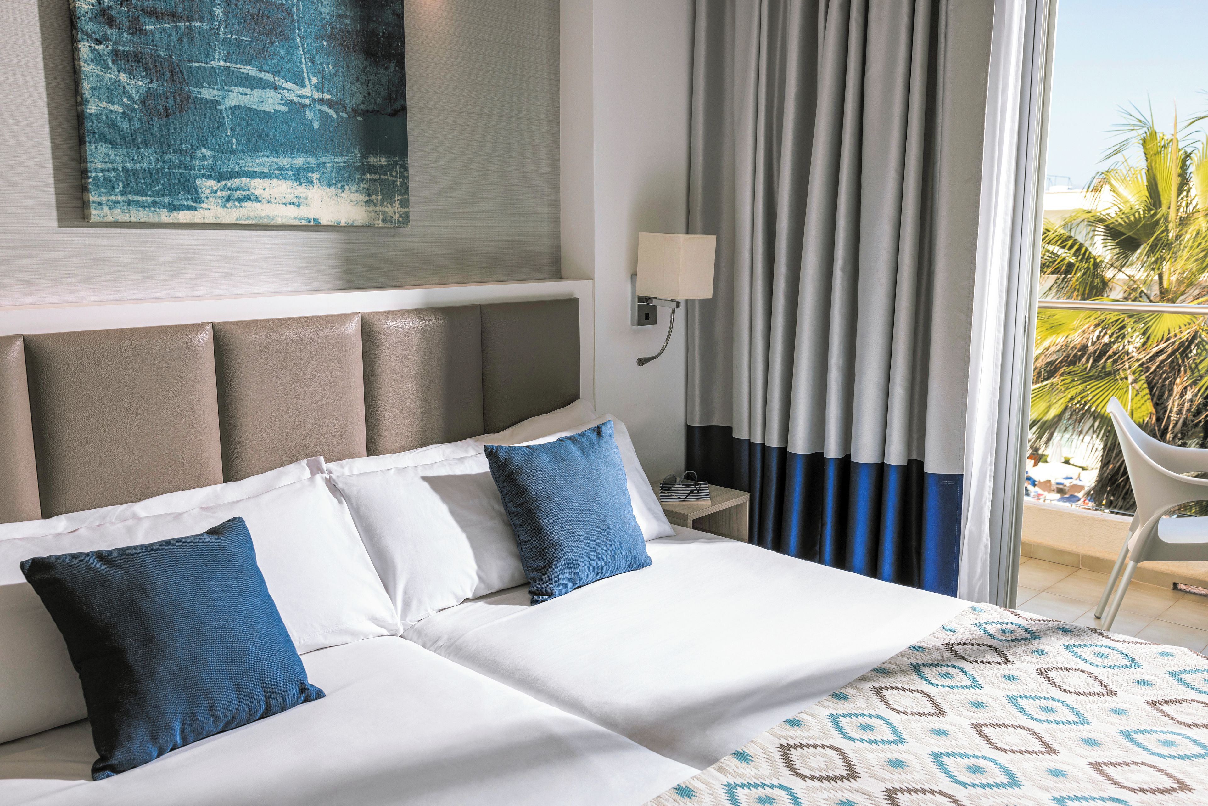 Una habitación de hotel con una cama, una mesita de noche, una lámpara y vistas al exterior.