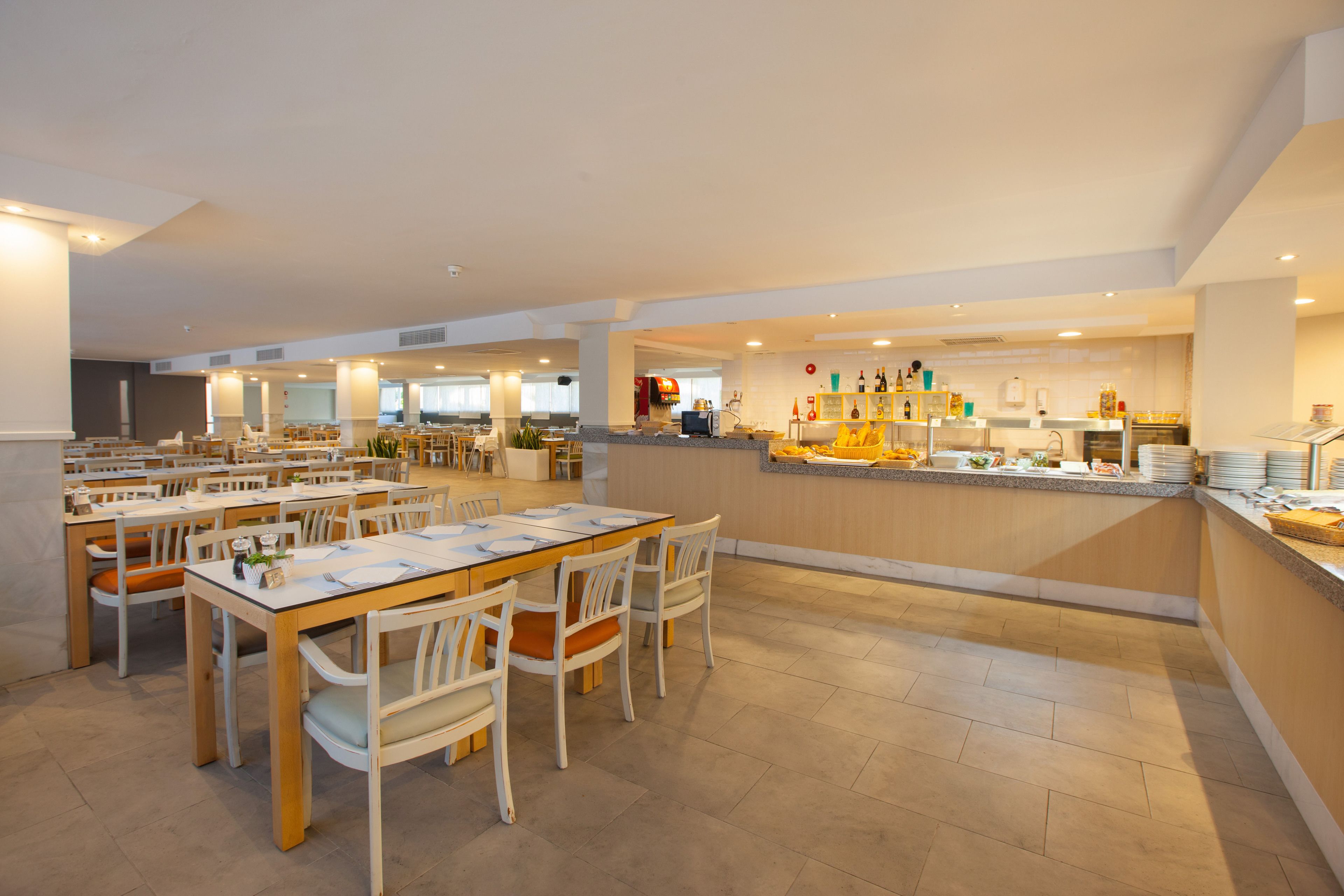 A spacious dining area with multiple tables and chairs, a central bar area with a counter, and a buffet setup.