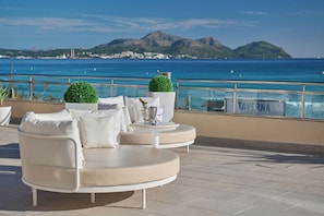 Una terraza con zona de estar, una mesa con una botella y vasos, y vistas al mar y a las montañas.