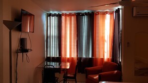 Une petite pièce avec une table, deux chaises, un canapé rouge et un téléviseur fixé au mur.
