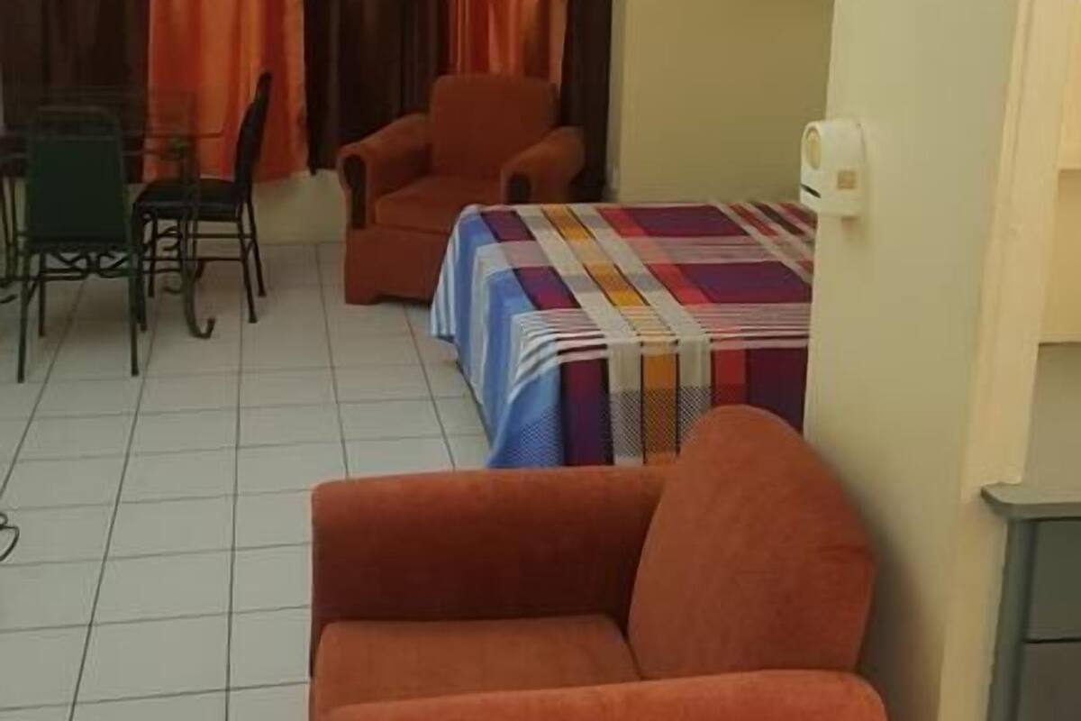 A small, well-lit room with a single orange chair, a table with a colorful tablecloth, and a ceiling fan.