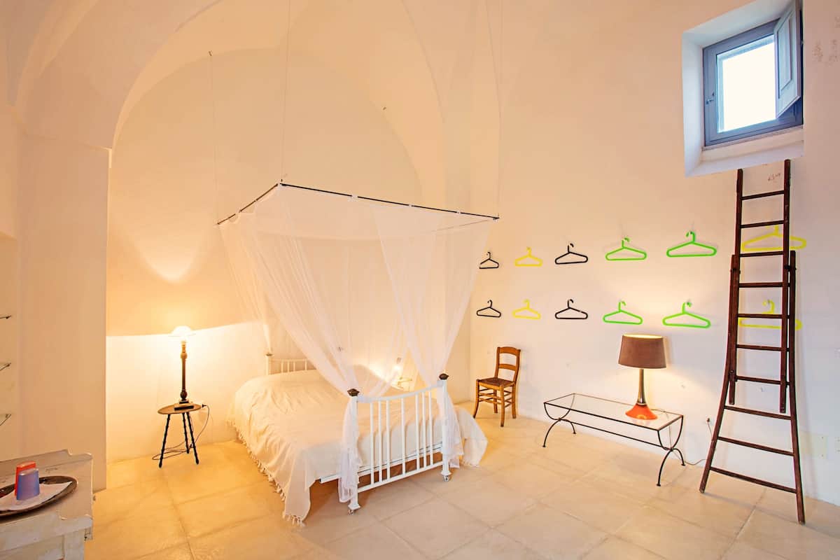Ein Schlafzimmer mit Baldachinbett, einem kleinen Tisch mit Lampe, einem Sessel, einer Leiter und Wandhaken.