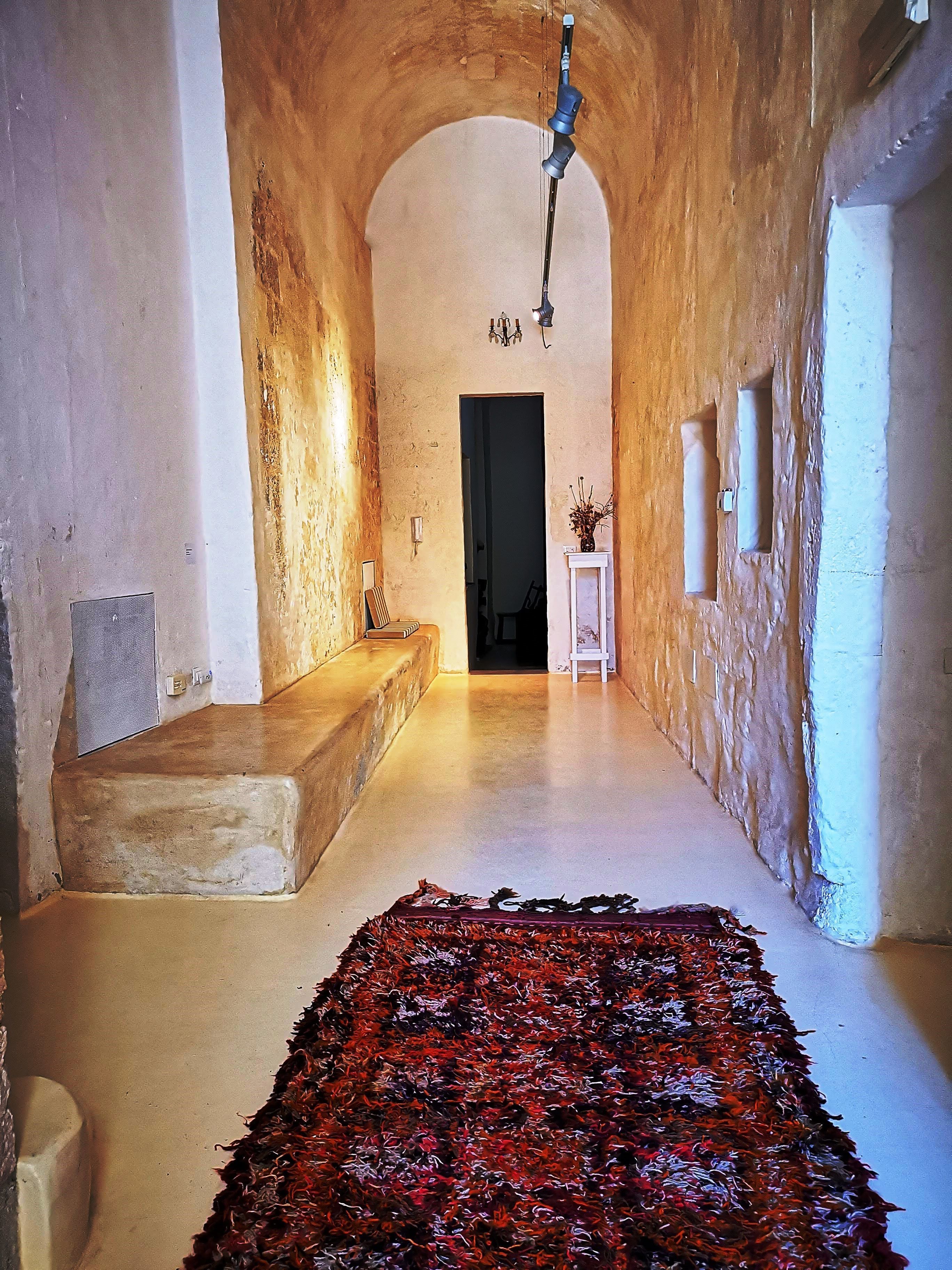 A narrow hallway with a rustic stone wall, a bench, and a patterned rug.