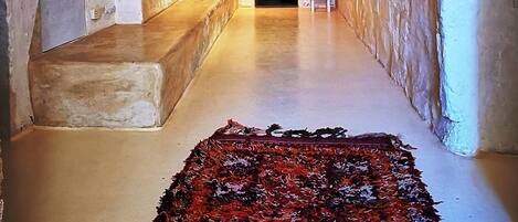 A narrow hallway with a rustic stone wall, a bench, and a patterned rug.