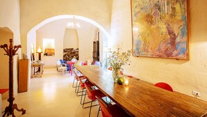 Un espace repas avec une longue table en bois, des chaises rouges et un grand tableau abstrait accroché au mur.