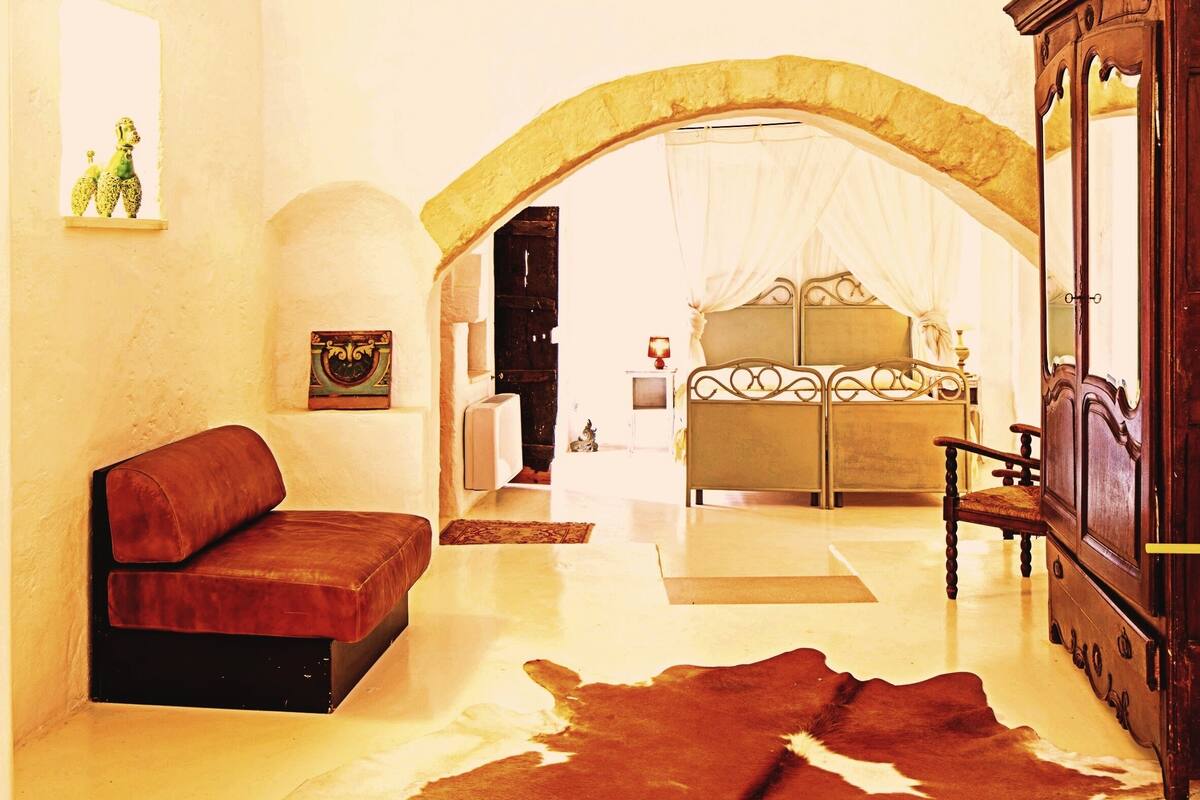 Ein Zimmer mit Kuhfellteppich, einer Couch, einem Bett mit Baldachin und einem Holzkasten.