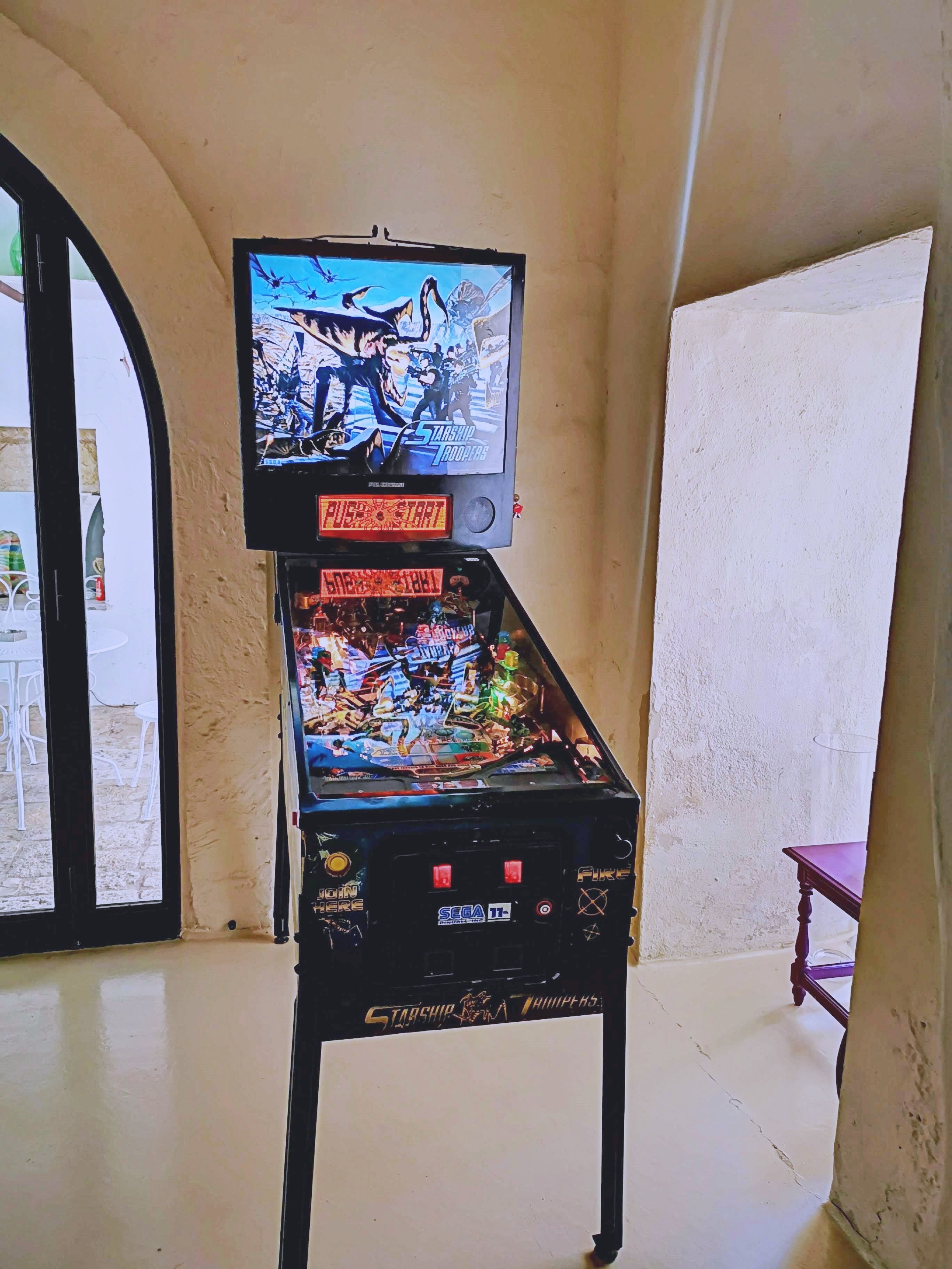 A pinball machine with a television mounted above it, set against a plain wall.