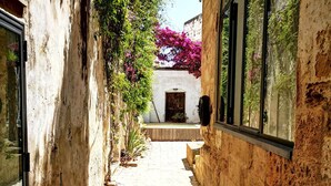 Un étroit sentier de pierre mène à un bâtiment traditionnel doté d’une porte en bois et d’une fenêtre donnant sur un jardin.