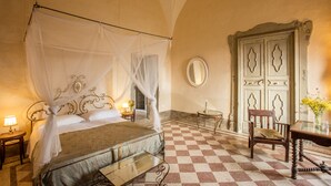Une pièce avec un lit sous un dais, une chaise en bois, une table avec un vase et une porte ornée de panneaux décoratifs.