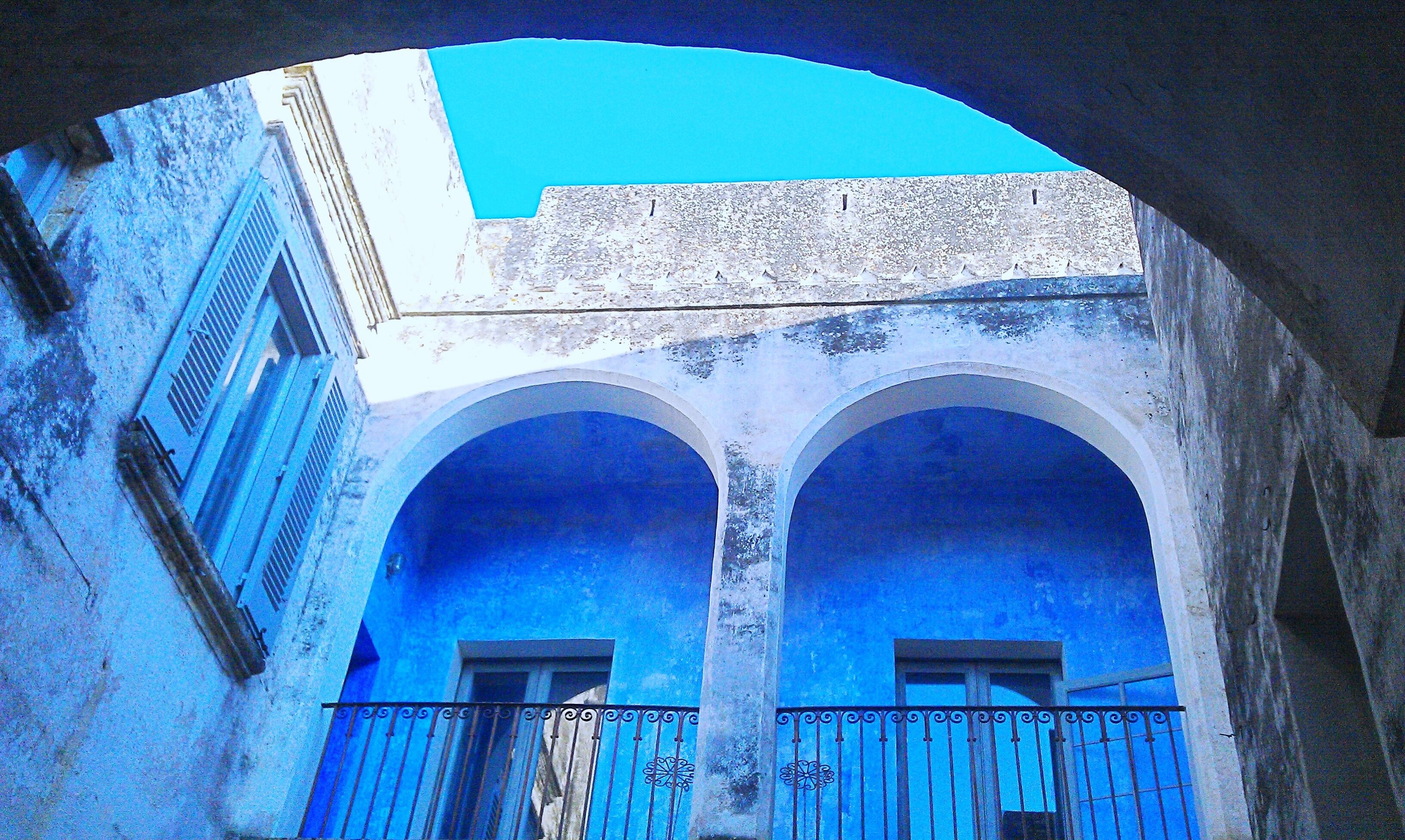 Um corredor arqueado com paredes pintadas de azul e um céu azul claro acima.