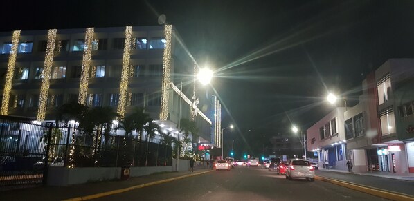 A street at night with buildings on either side, streetlights, and cars.