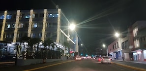 A street at night with buildings on either side, streetlights, and cars.