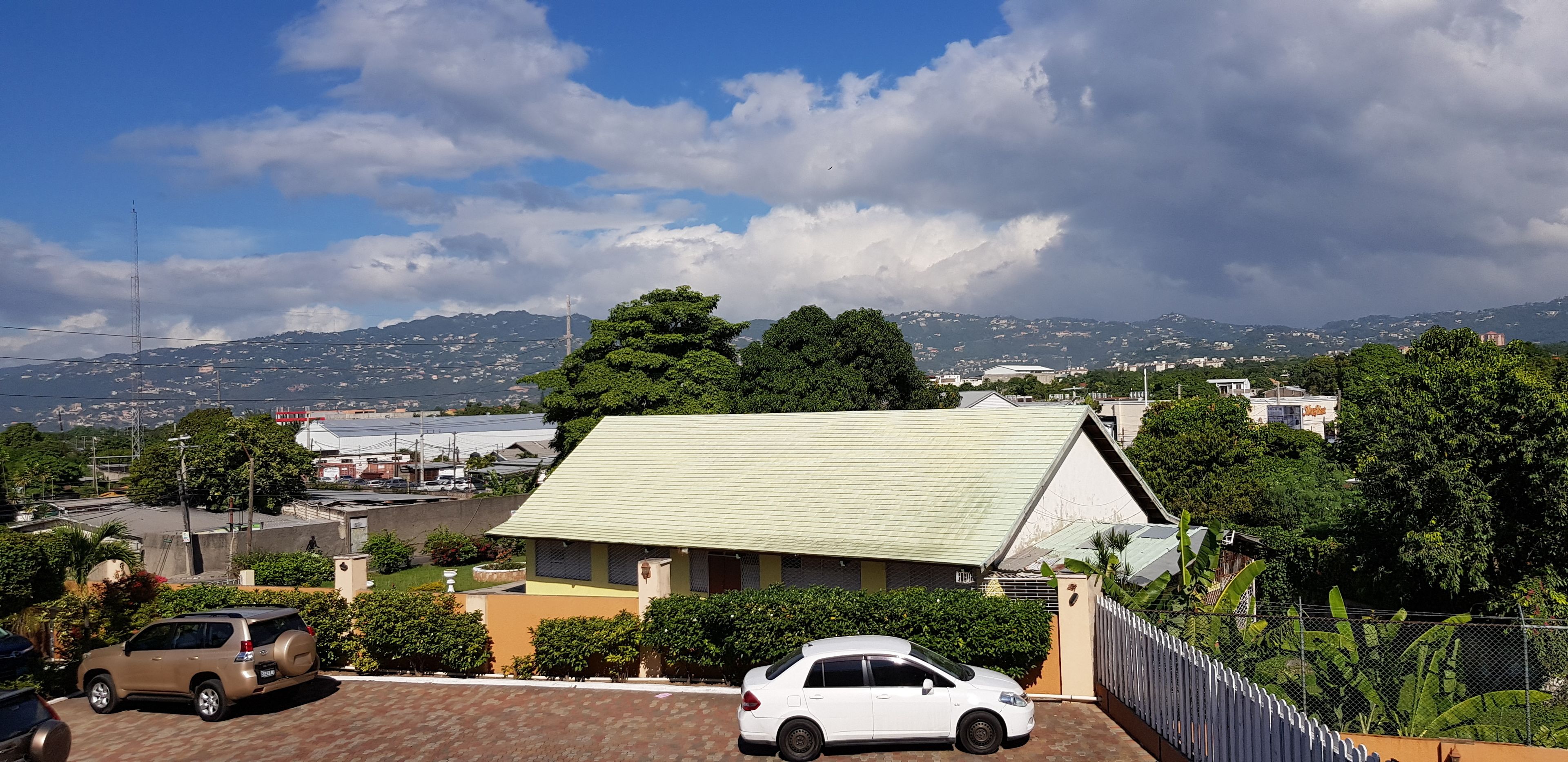 Un barrio residencial con una casa que tiene techo verde, rodeada de abundante vegetación y un cielo despejado.