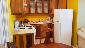 Ett kompakt kök med träskåp, en vit spis, ett kylskåp och ett matbord med stolar.