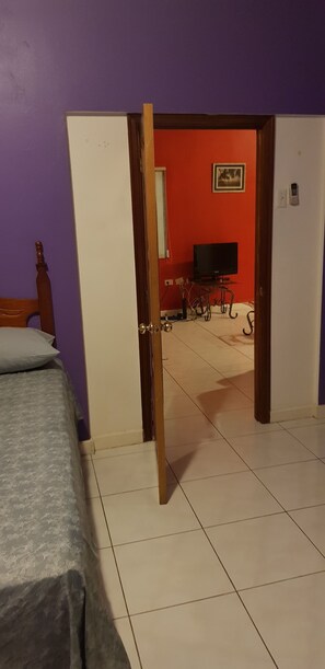 A room with a bed, a television, and a door leading to another room.
