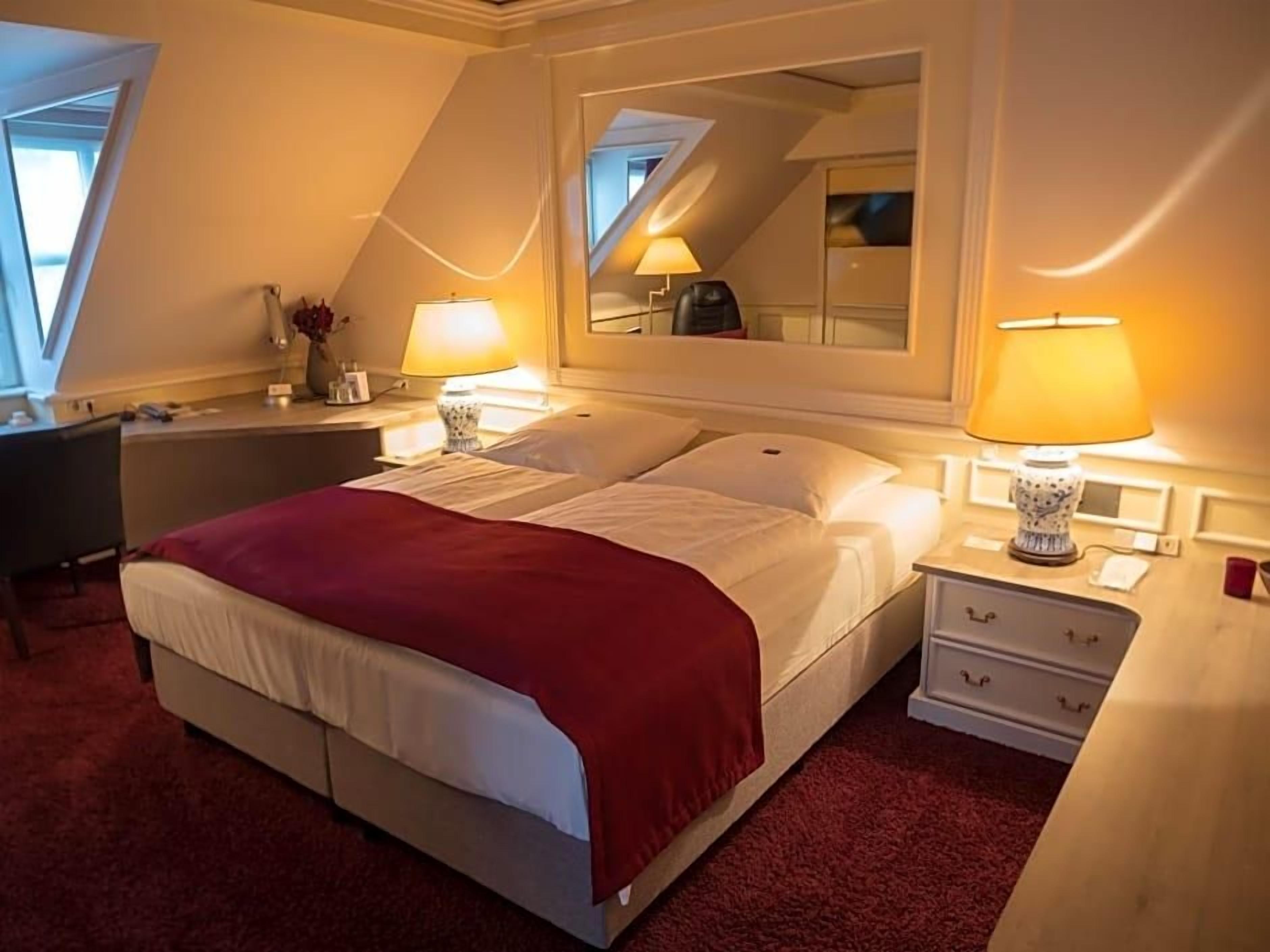 Ein Hotelzimmer mit einem Bett, Nachttischen mit Lampen, einem Schreibtisch und einem Spiegel.