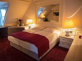 A hotel room with a bed, bedside lamps, a desk, and a mirror.