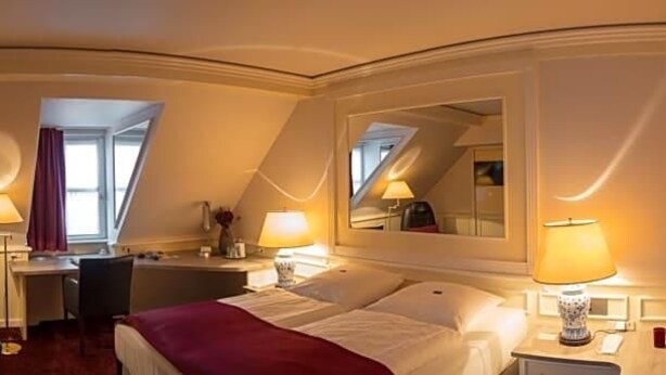 A hotel room with a bed, desk, chair, lamps, and a mirror.