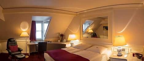 Une chambre d’hôtel équipée d’un lit, d’un bureau, d’une chaise, de lampes et d’un miroir.
