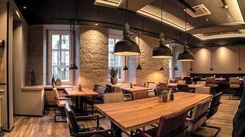 Ein Restaurantinneres mit Holztischen und -stühlen, Pendelleuchten und einer Wand mit Natursteinverkleidung.