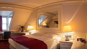 A hotel room with a bed, desk, chair, and a large mirror.