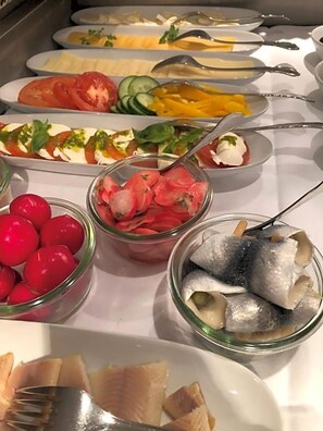 Un bufé con diversos alimentos, incluyendo pescado, tomates, pepinos y queso.