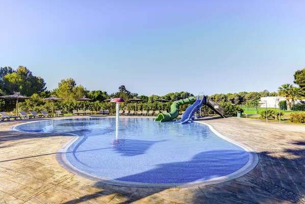 Una piscina con tobogán, tumbonas y sombrillas.