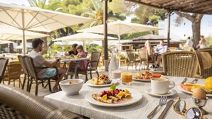 An outdoor dining area with tables, chairs, umbrellas, and a variety of breakfast items.
