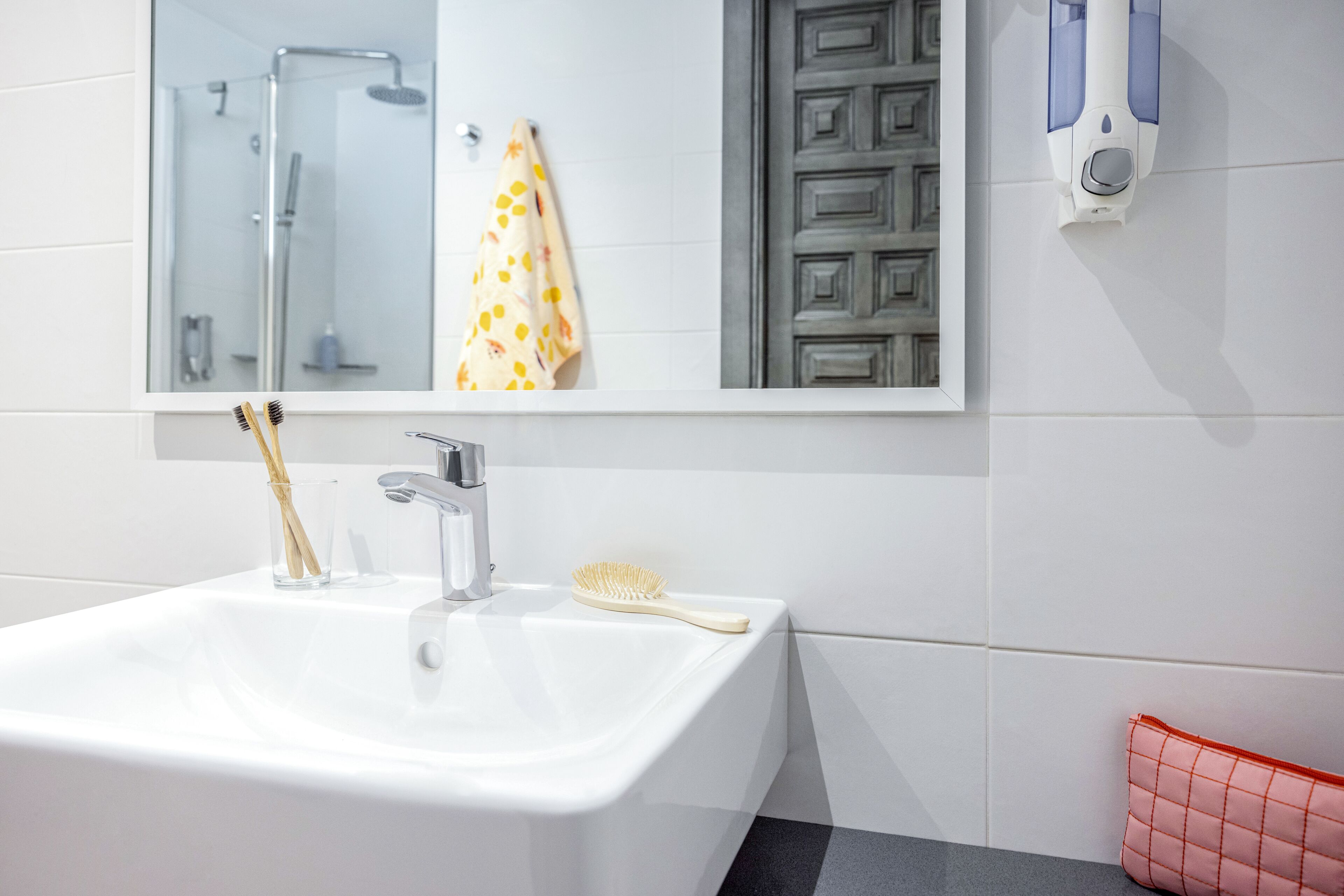 A bathroom with a white sink, a mirror, a shower, and a towel rack.