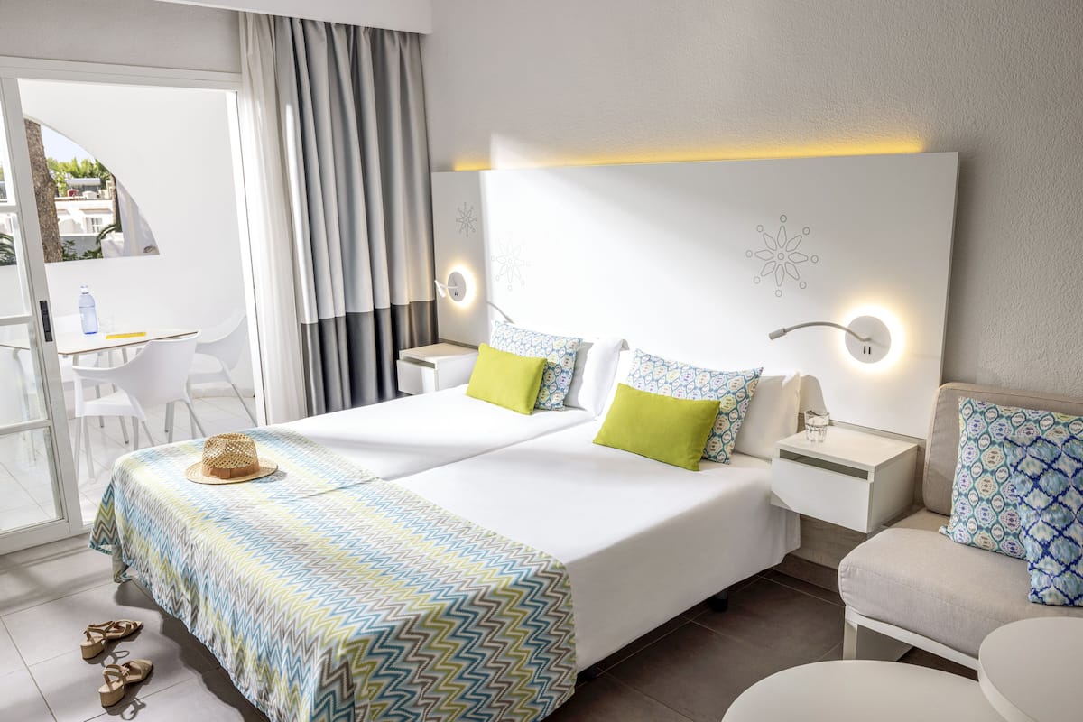 A hotel room with a large bed, two bedside tables, a small table with chairs, and a view of the outdoors.