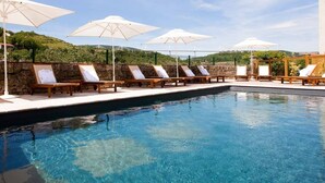 A poolside area with lounge chairs and umbrellas, a stone wall, and a view of the hills. - Château de Creissels (Creissels)